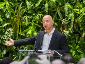 jeff bezos - fundador da Amazon de terno preto com camisa cinza enquanto fala aparentemente em uma palestra