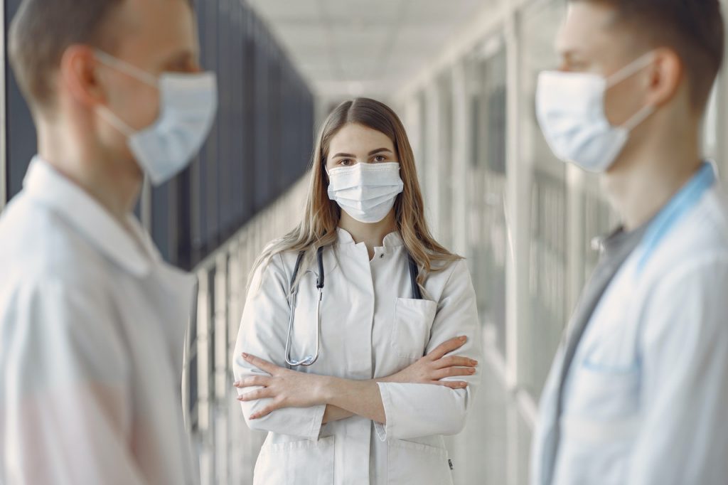 três profissionais de enfermagem se olhando com jalecos e máscaras no rosto