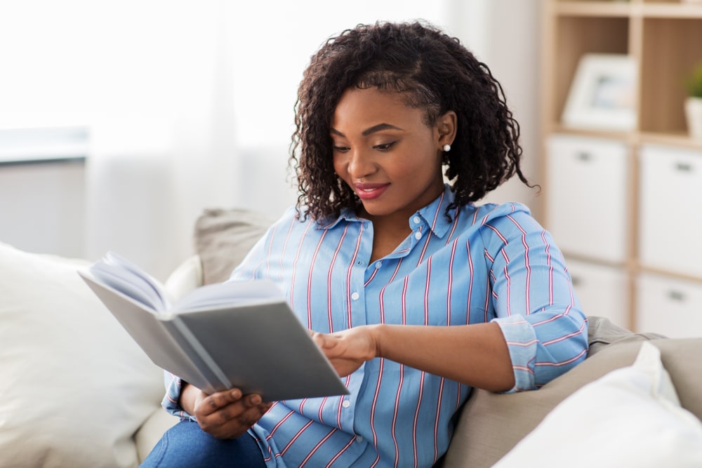 mulher sentada no sofá com um livro na mão para ilustrar texto com dicas para ler mais