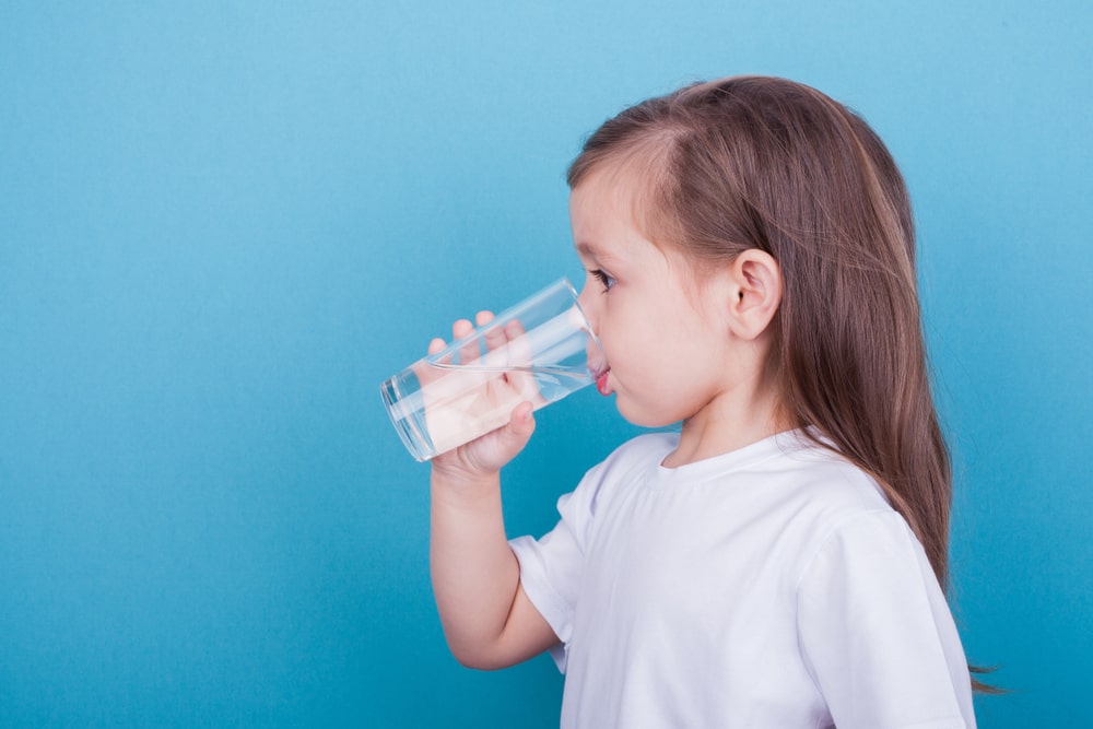 criança de lado bebendo copo de água