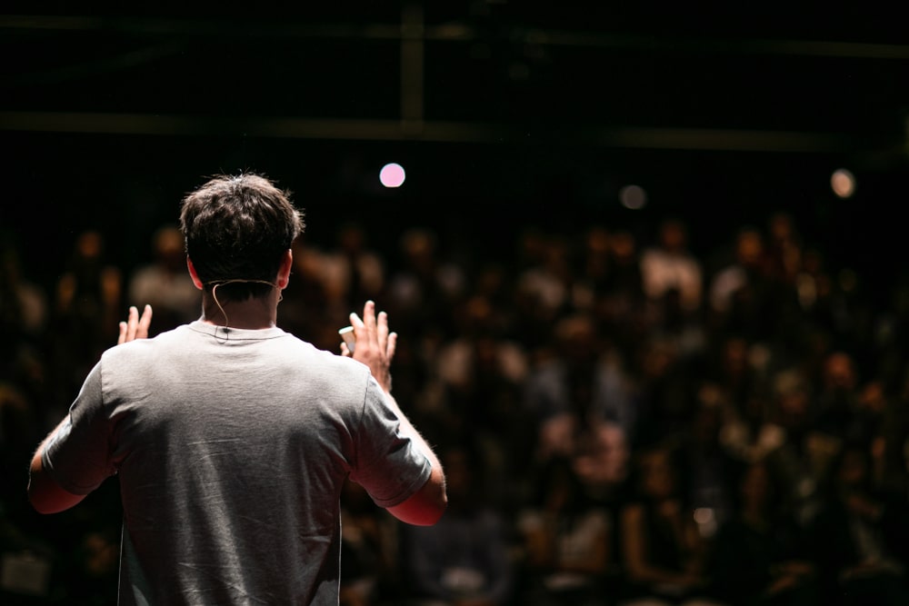 homem de costas com uma plateia em sua frente para ilustrar texto sobre como falar em público