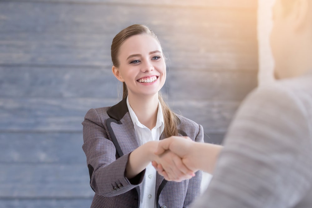 mulher cumprimentando outra pessoa com aperto de mão para ilustrar texto sobre como passar na segunda etapa da entrevista de emprego