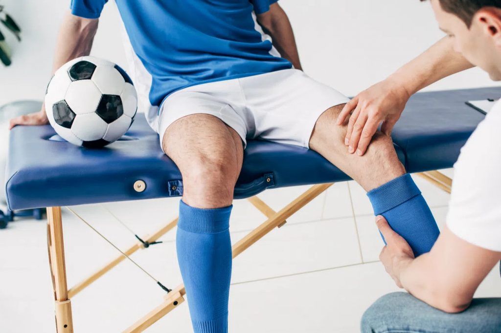 fisioterapeuta com a mão no joelho de jogador de futebol para ilustrar texto sobre Fisioterapia do Esporte