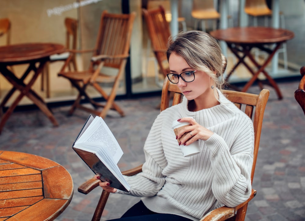 mulher lendo livro com café na mão para ilustrar texto sobre habilidade de negociação