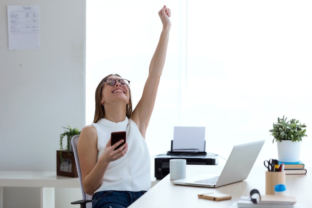 mulher comemorando com o braço esquerdo para cima em ambiente de escritório para ilustrar texto sobre dicas para processo seletivo