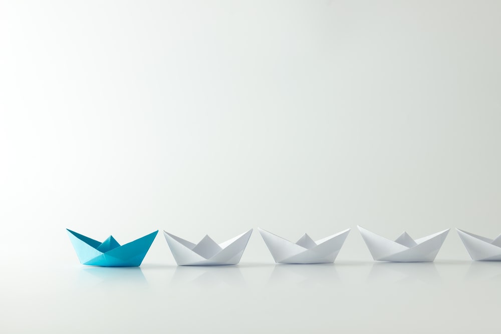 barcos de papel com azul em destaque para ilustrar texto sobre primeiro cargo de liderança