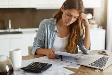 mulher olhando para contas e calculadora para ilustrar texto sobre como ter organização financeira