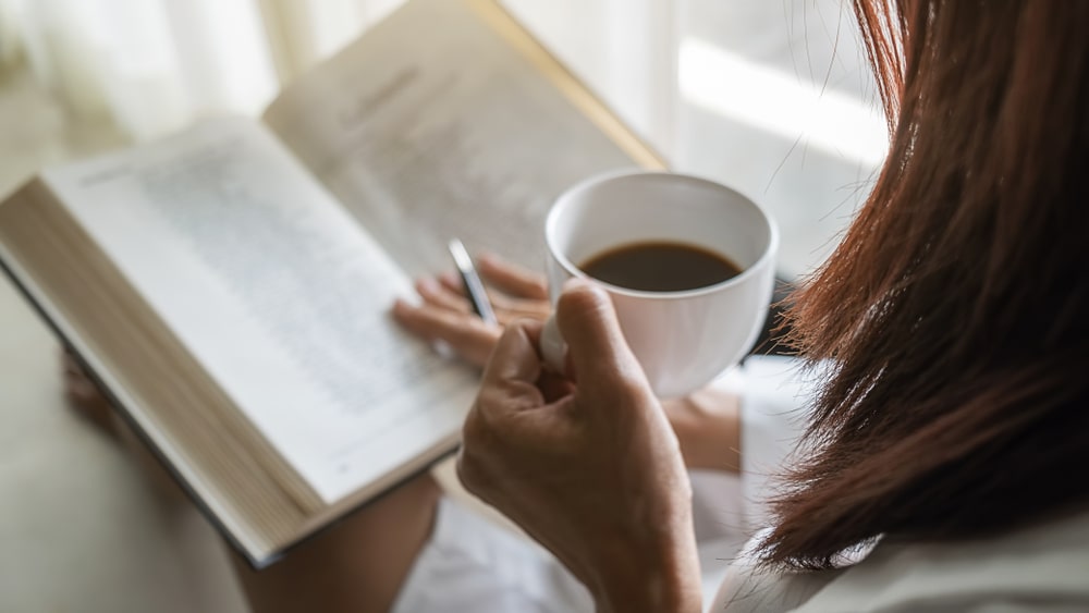 mulher com xícara de café e livro para ilustrar texto sobre como interpretar um texto corretamente