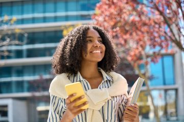 jovem sorrindo com celular na mão para ilustrar texto sobre qual a melhor faculdade para fazer pós-graduação
