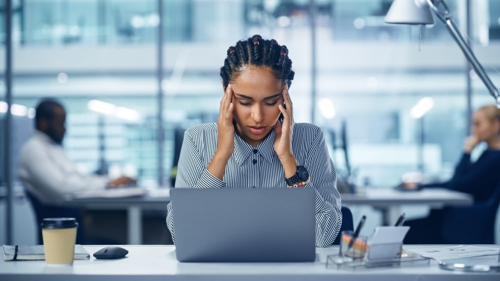 mulher com expressão de dor de cabeça para ilustrar texto sobre desgaste no trabalho