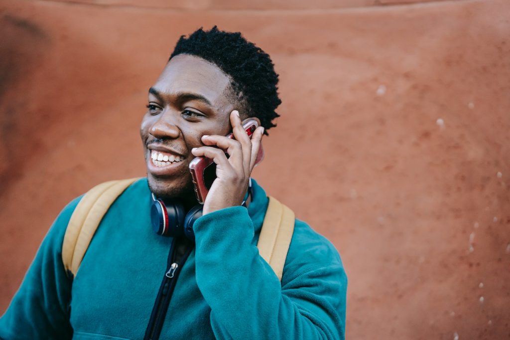 homem negro vestindo uma blusa manga longa azul sorrindo ao telefone