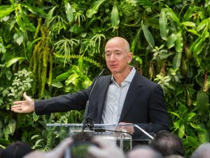 jeff bezos - fundador da Amazon de terno preto com camisa cinza enquanto fala aparentemente em uma palestra