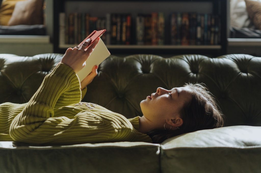 Jovem deitada em cima da cama lendo um livro