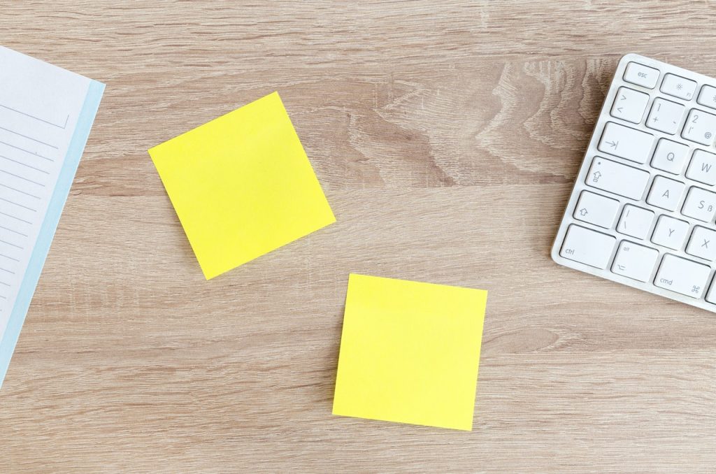 uma folha, dois post-it e um teclado sob uma mesa de madeira