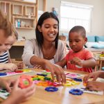 professora em sala de aula ao lado de alunos da Educação Infantil