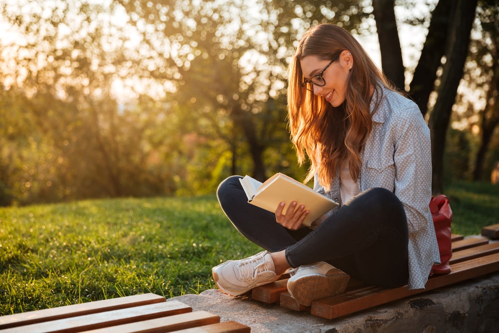 mulher ao ar livre lendo livro para ilustrar texto sobre livros para crescimento pessoal