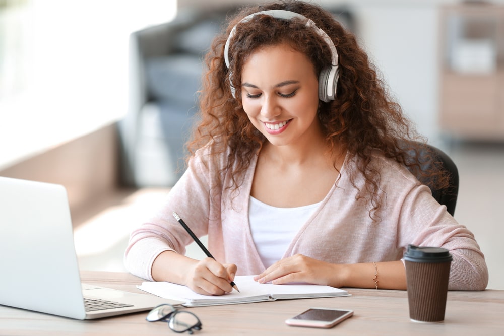 mulher com fone de ouvido fazendo anotações para ilustrar conteúdo sobre bolsa de estudo da pós-graduação