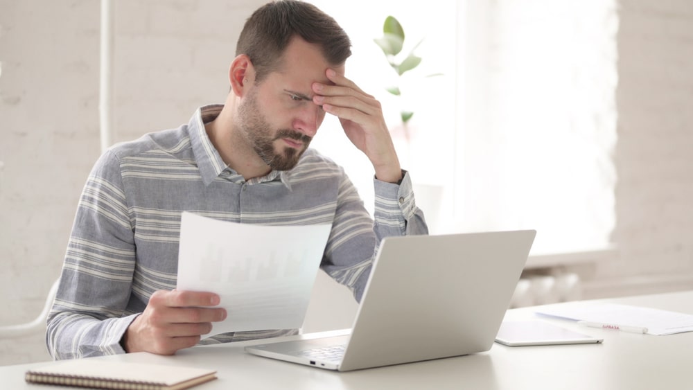 homem com mão na testa e outra segurando um papel para ilustrar texto sobre estresse no ambiente de trabalho