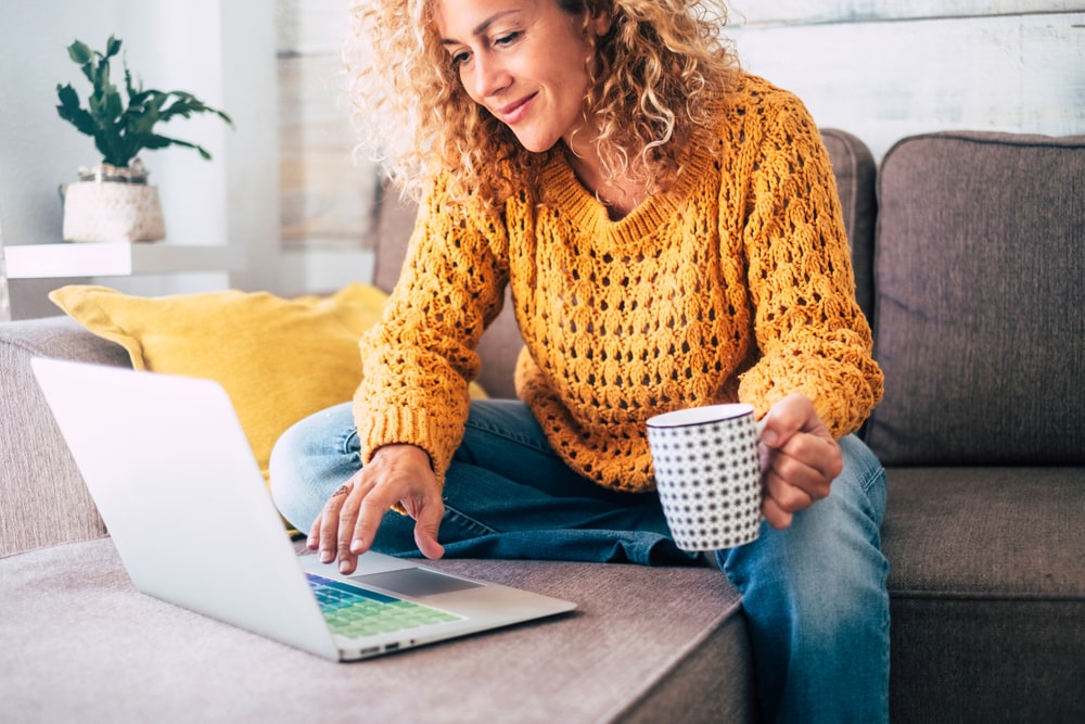 mulher sentada no sofá com notebook para ilustrar texto sobre investimentos para a Black Friday