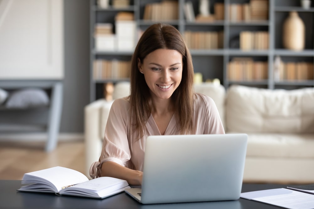 mulher feliz digitando no notebook para ilustrar texto sobre busca por especialistas e importância da pós-graduação