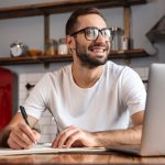 homem sorrindo e estudando online para ilustrar texto sobre como fazer pós-graduação