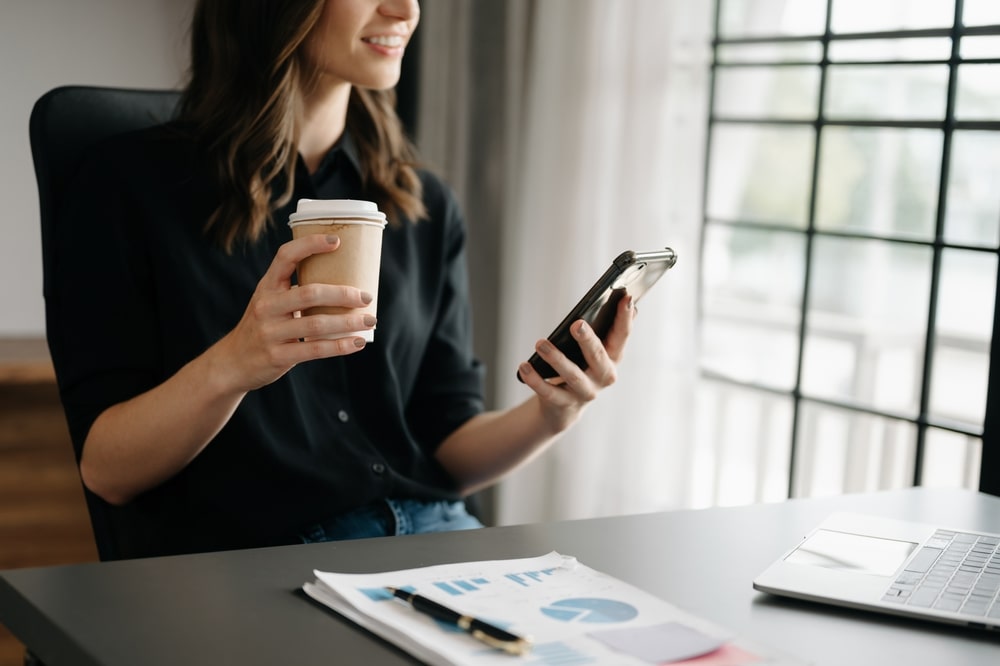 mulher com celular na mão para ilustrar texto sobre frases para se apresentar no grupo do WhatsApp do trabalho