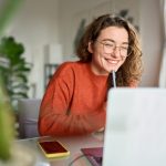 mulher sorrindo com notebook para ilustrar texto sobre pós-graduação com TCC opcional