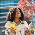 jovem sorrindo com celular na mão para ilustrar texto sobre qual a melhor faculdade para fazer pós-graduação