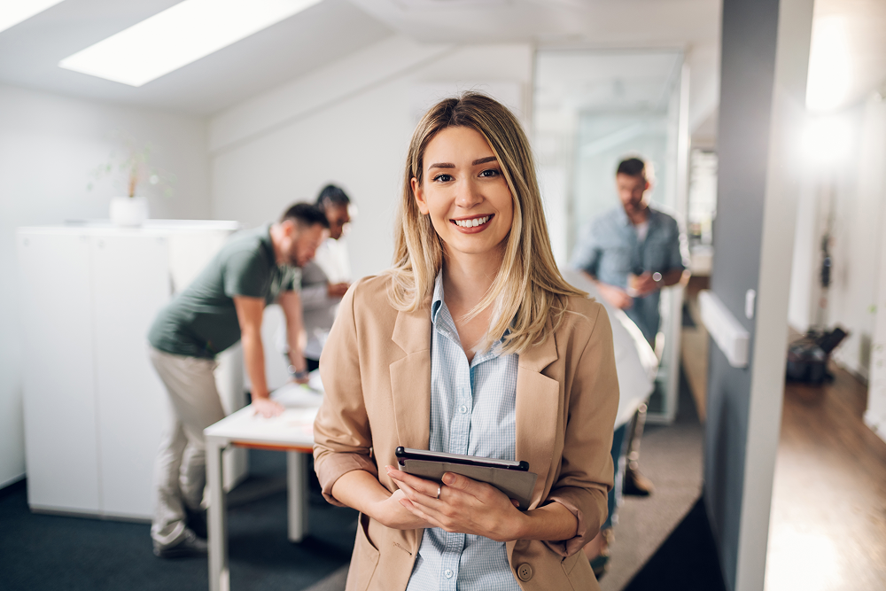 Mulher em um escritório sorri para a foto. Importância do líder no trabalho em equipe